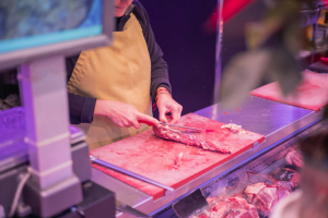 A specialist halal butcher cutting fresh beef to order at the counter beside pre-packed supermarket trays